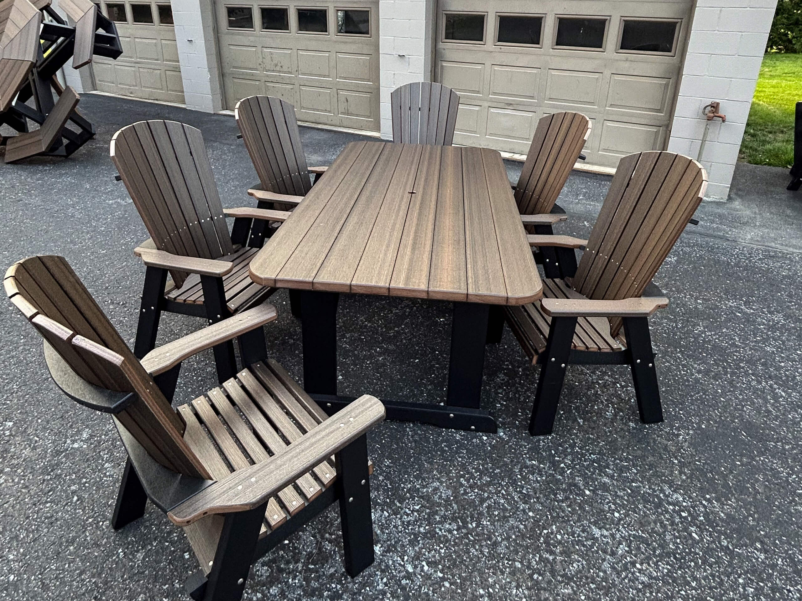 Oregan Lawn Furniture Leola, Pa Rectangular outdoor table with six matching wooden chairs arranged around it, positioned on a paved surface in front of a garage building.