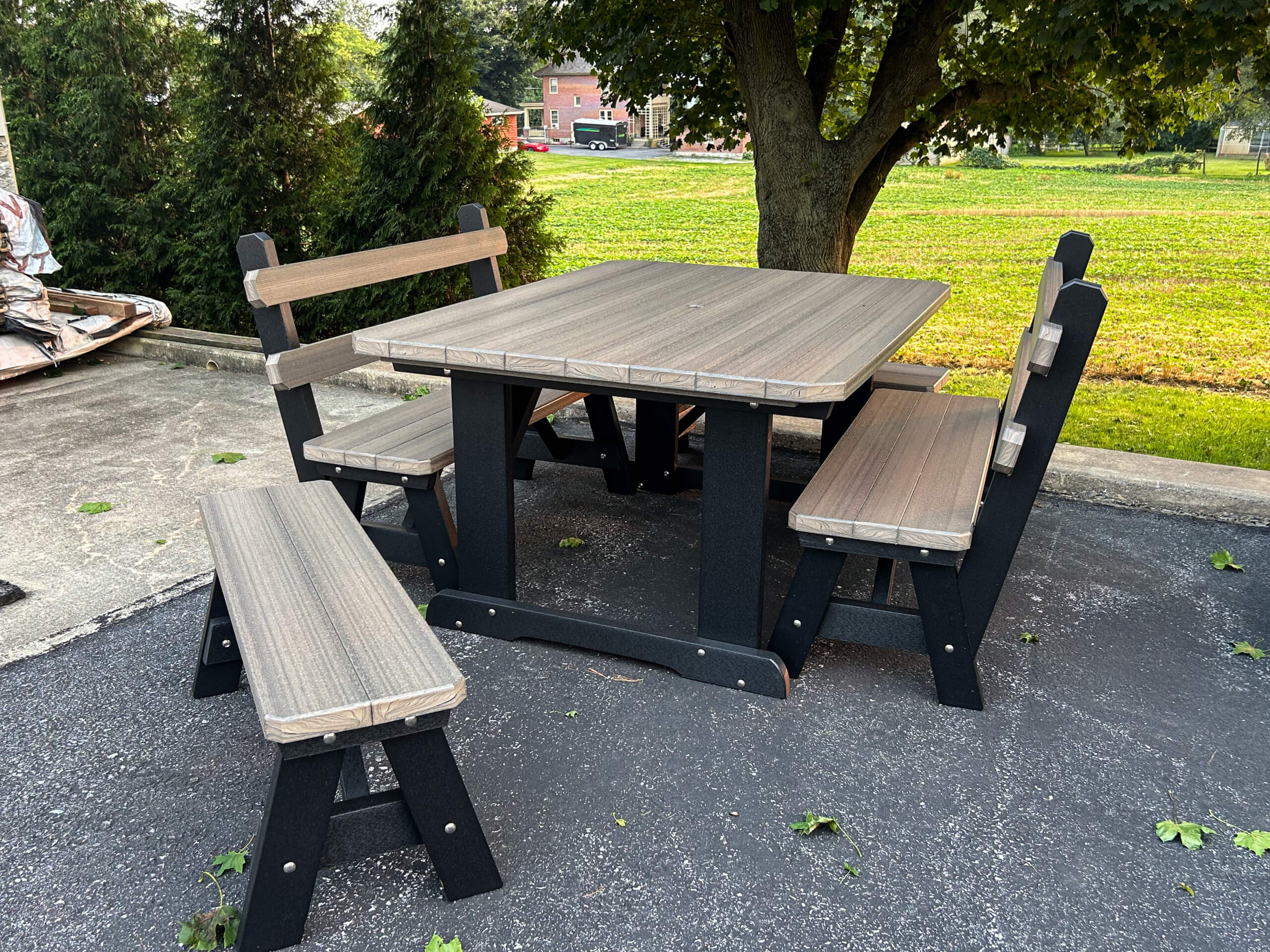 Oregan Lawn Furniture Leola, Pa A wooden outdoor table set with two benches and two chairs is placed on a paved patio near a tree and a grassy area.