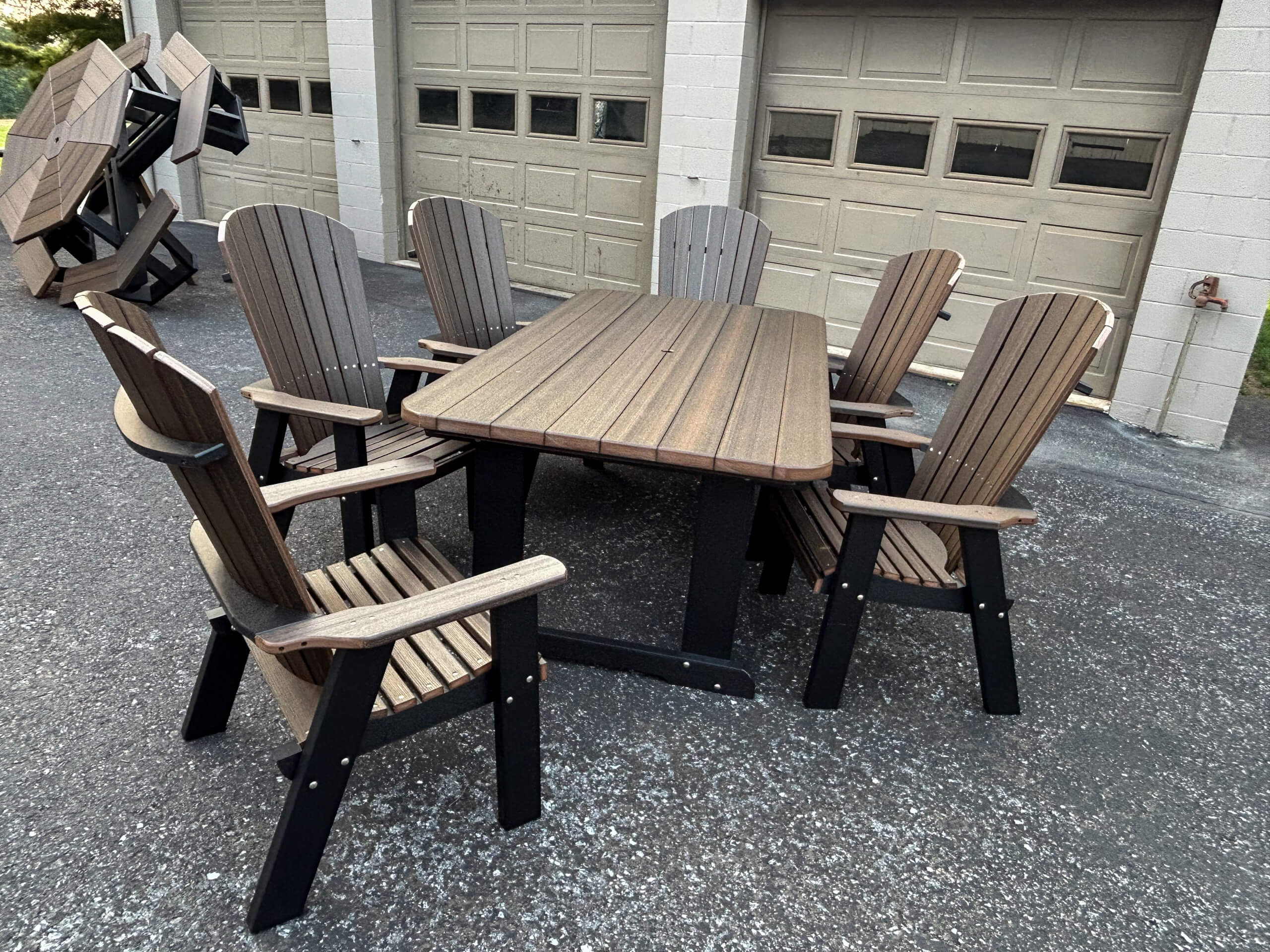 Oregan Lawn Furniture Leola, Pa A wooden outdoor table with six matching chairs is set on an asphalt surface in front of a building with closed garage doors.