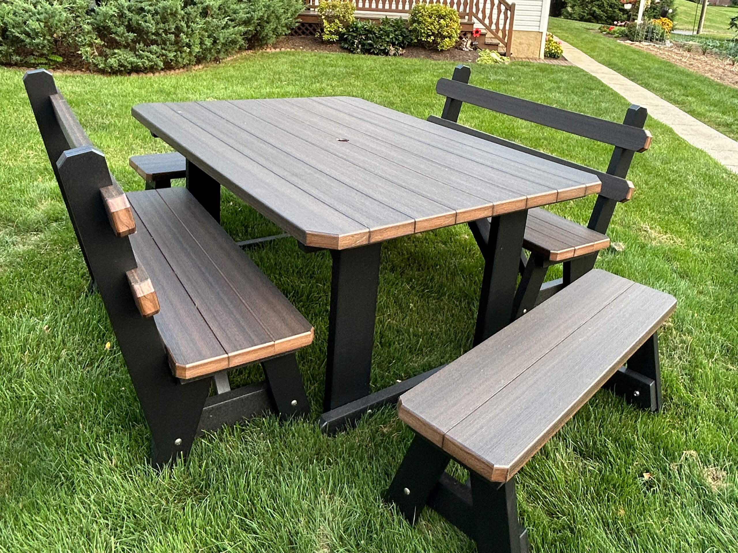 Oregan Lawn Furniture Leola, Pa Outdoor wooden picnic table with two benches and one bench with a backrest, placed on a grassy lawn near shrubs and a walkway.