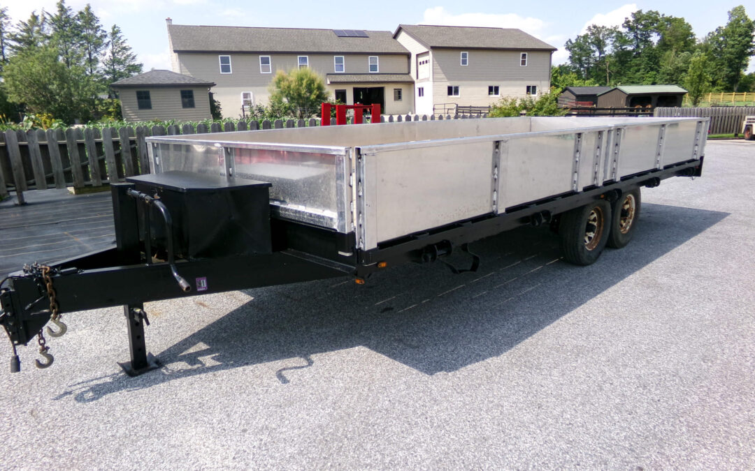 9.9.26 Nickel Mine Welding Gallery 2-10 A large flatbed utility trailer with metal side panels is parked on a gravel surface in front of a fenced residential property.
