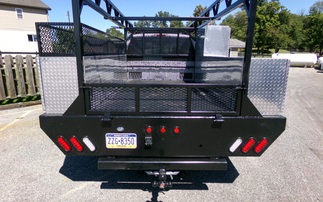 9.9.26 Nickel Mine Welding Gallery 2-11 Rear view of a black utility truck bed with mesh sides, diamond plate toolboxes, red lights, and a ZZG-8350 license plate, parked on pavement near houses and trees.