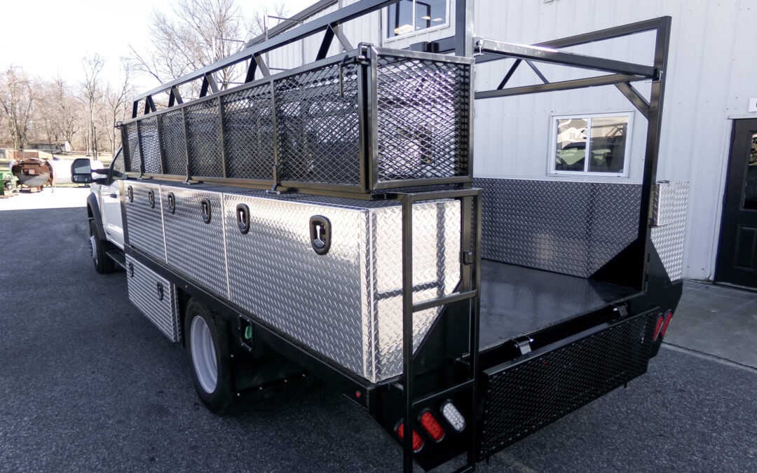 9.9.26 Nickel Mine Welding Gallery 2-2 Flatbed utility truck with diamond plate toolboxes, metal mesh racks, and rear gate, parked outside a white industrial building.