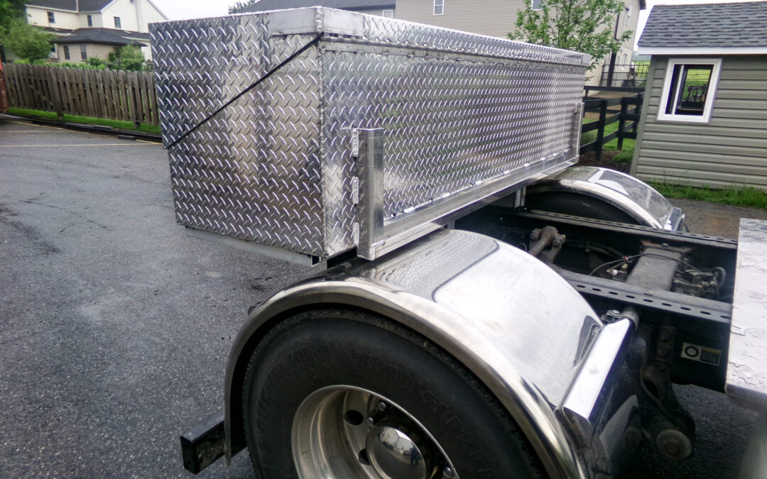 9.9.26 Nickel Mine Welding Gallery 2-3 Diamond plate aluminum storage box mounted above the rear wheels of a semi-truck, with houses and sheds visible in the background.